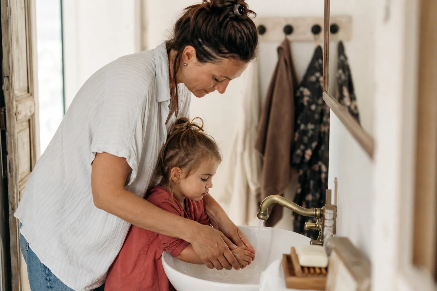 Parent lavant doucement les mains de son enfant avec un savon au lait de chèvre, dans une salle de bain lumineuse.