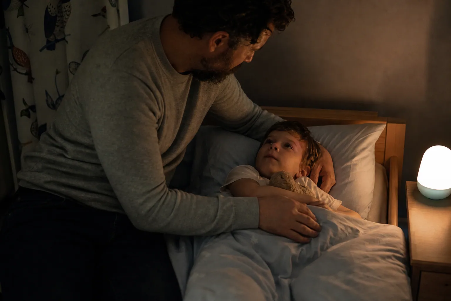 Parent assis au bord du lit d'un enfant la nuit dans une chambre à la lumière tamisée