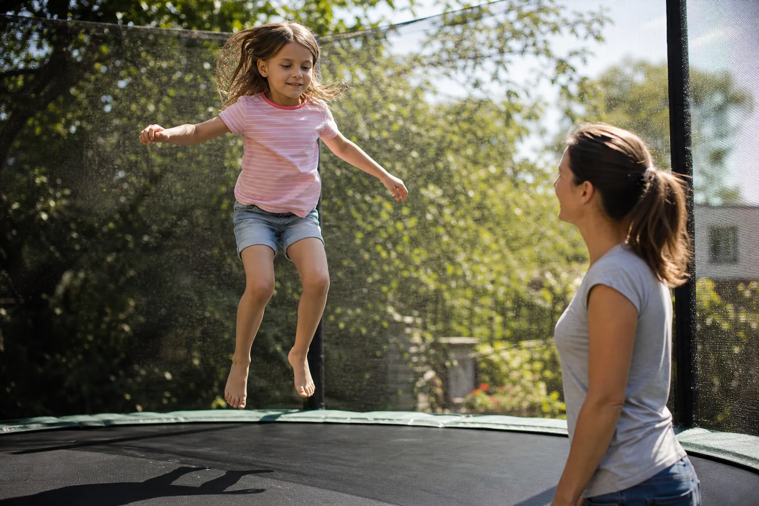 Un enfant saute sur un trampoline muni d'un filet de sécurité, surveillé par un parent.