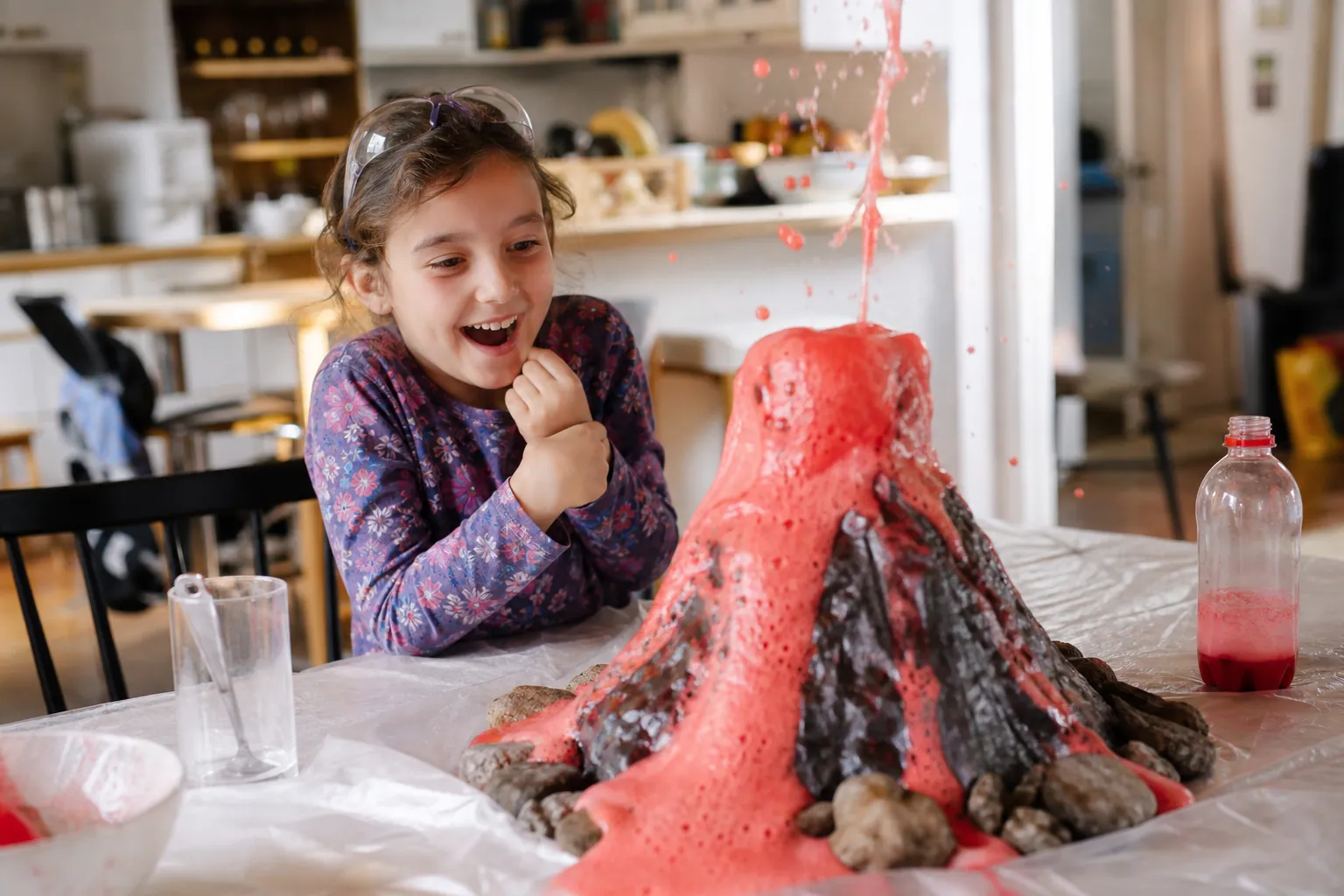 Un enfant observe avec émerveillement l'éruption mousseuse d'un volcan fait maison.